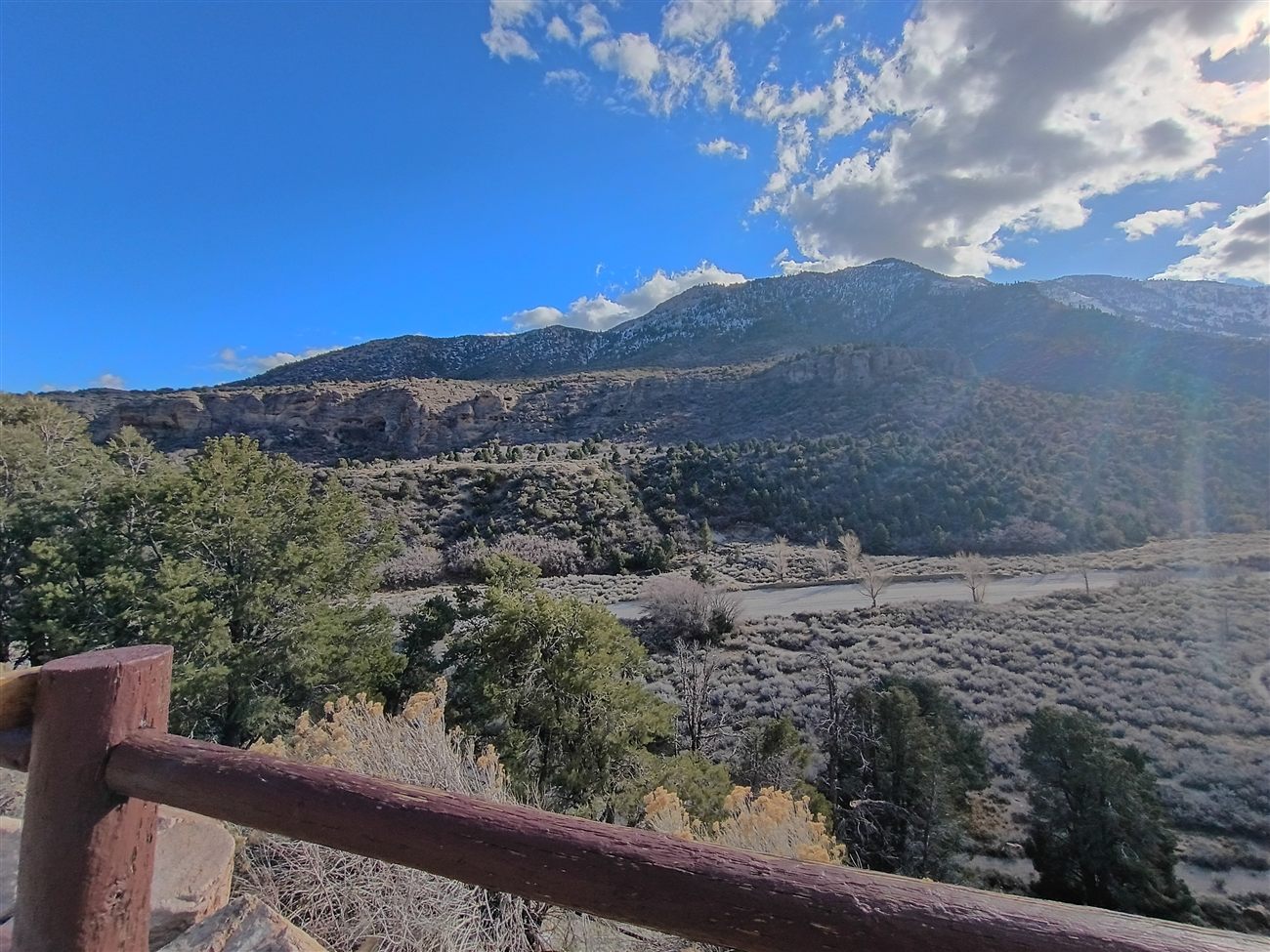 A view of snow-dusted mountains from a wooden deck railing