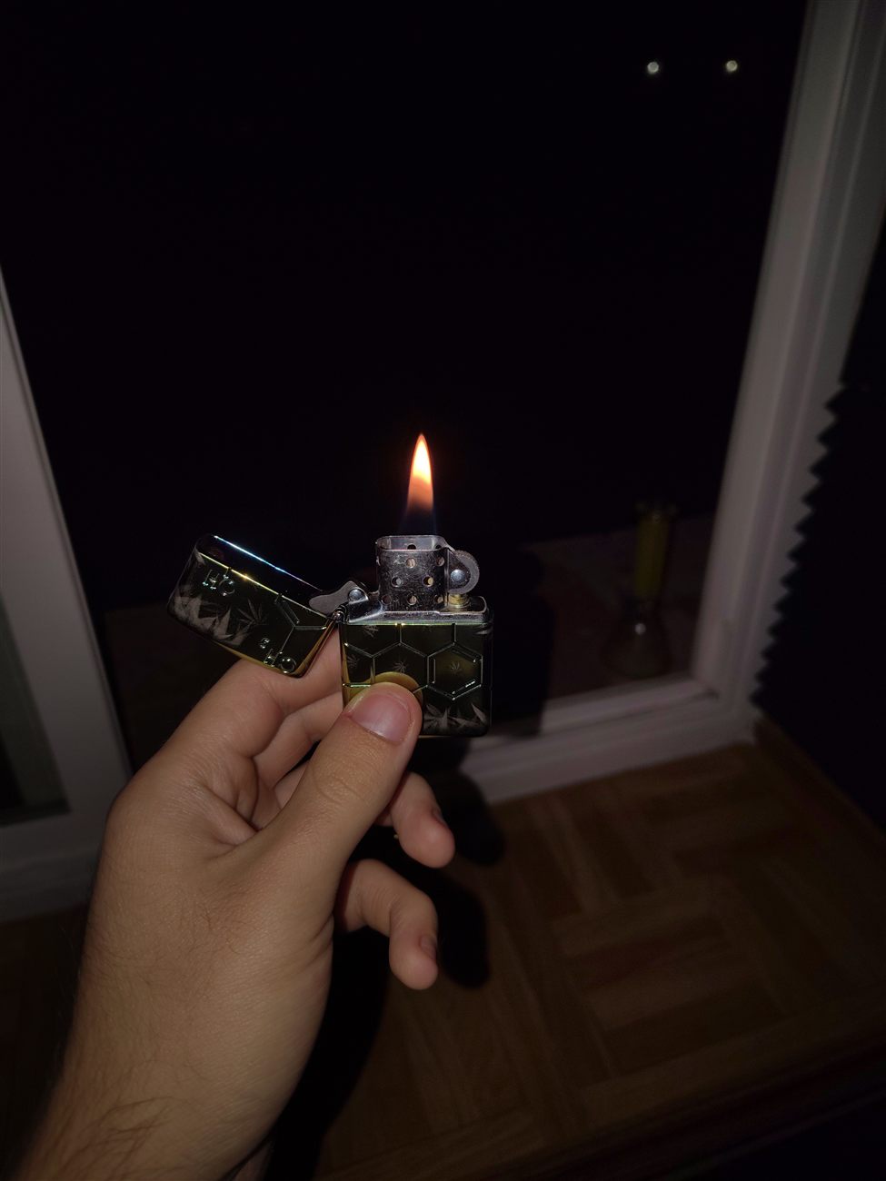 A silver hexagon-patterned Zippo lighter lit with a flame at night