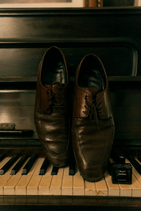 A bottle of Bleu de Chanel resting on piano keys next to leather shoes