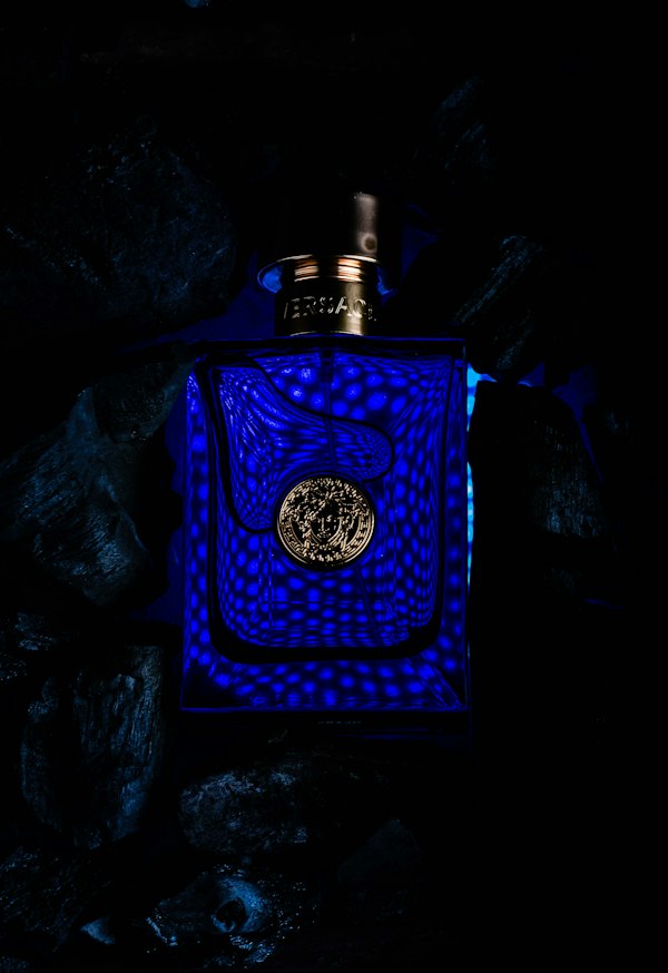 A bottle of Versace Dylan Blue lit blue against dark rocks